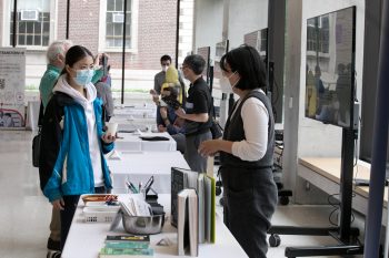 Two women wearing masks chat around an information display table.