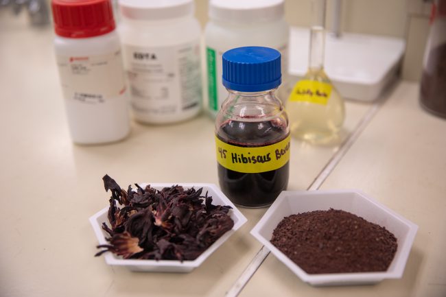 A bottle of a purple hibiscus beverage is shown next its ingredients