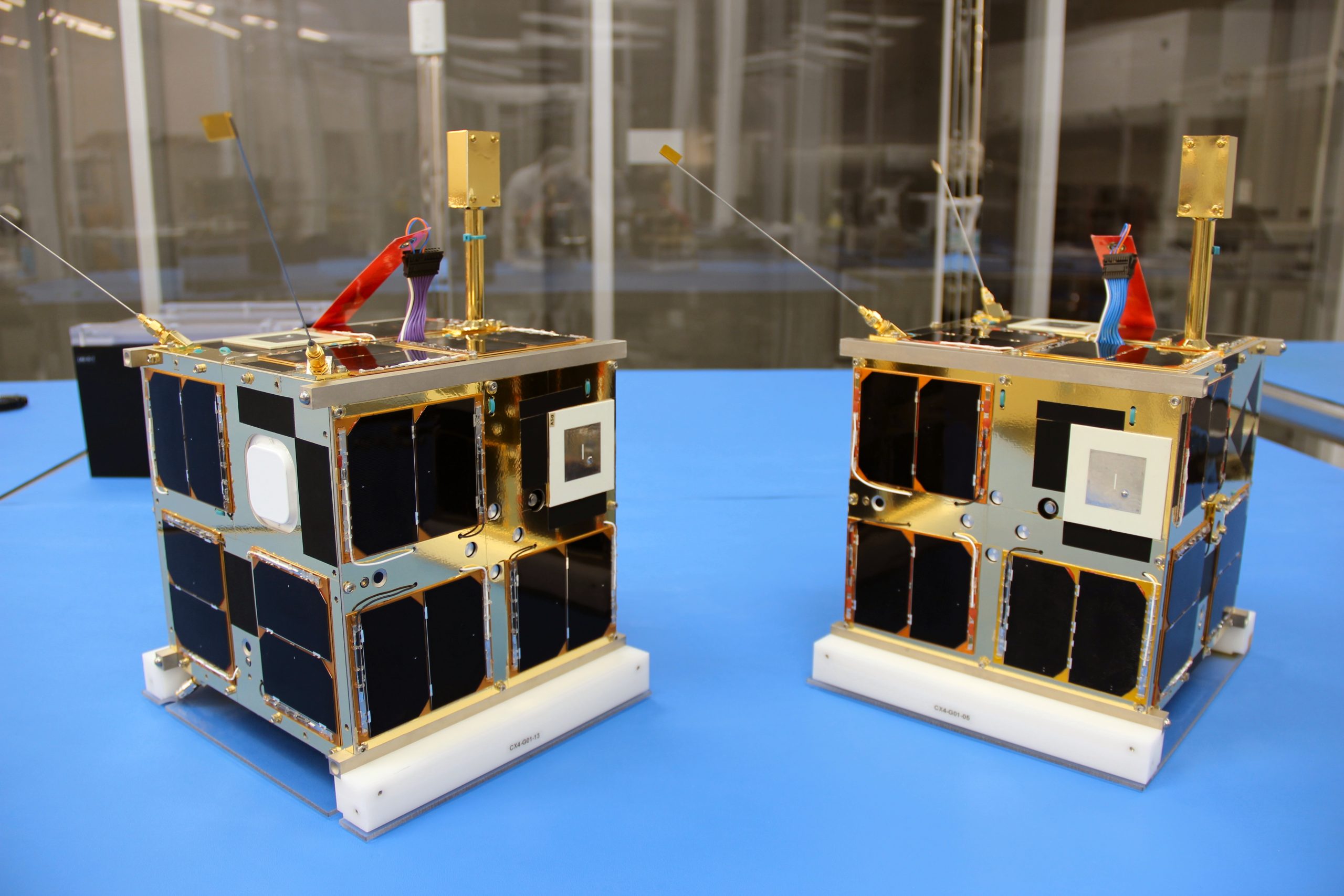 Two nanosatellites, 7 kg in size, sit on a blue table. 