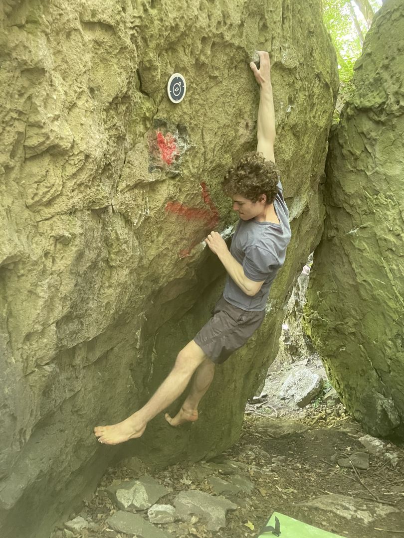 Man wearing grey shorts and shirt is bouldering, a form of rock climbing.