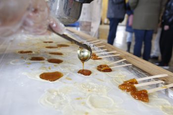 An individual pours maple syrup on an ice table. Several sticks of maple taffy are also on the table. 