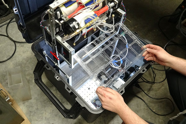 The experimental apparatus is packed inside a box measuring 50 cm x 50 cm x 50 cm and contains pumps and tubes that simulate the operation of a 3D printer. To simulate a molten thermoplastic, the team is using ordinary corn syrup. (Photo: Michael Lawee)