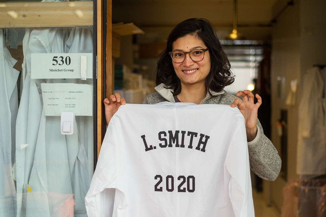 Laura Smith, a PhD student in chemical and biomedical engineering, holds up a lab coat bearing her name that will be hung in Molly Shoichet's lab following her graduation next year (photo by Geoffrey Vendeville)
