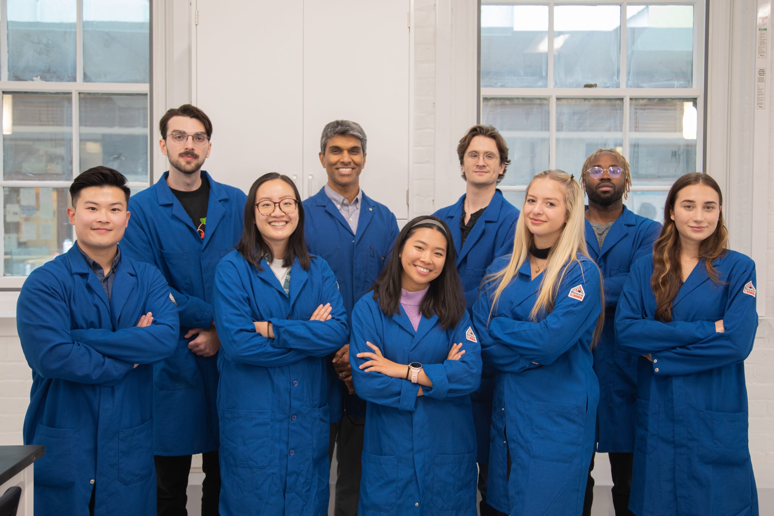 Two rows of scientists pose wearing blue lab coats