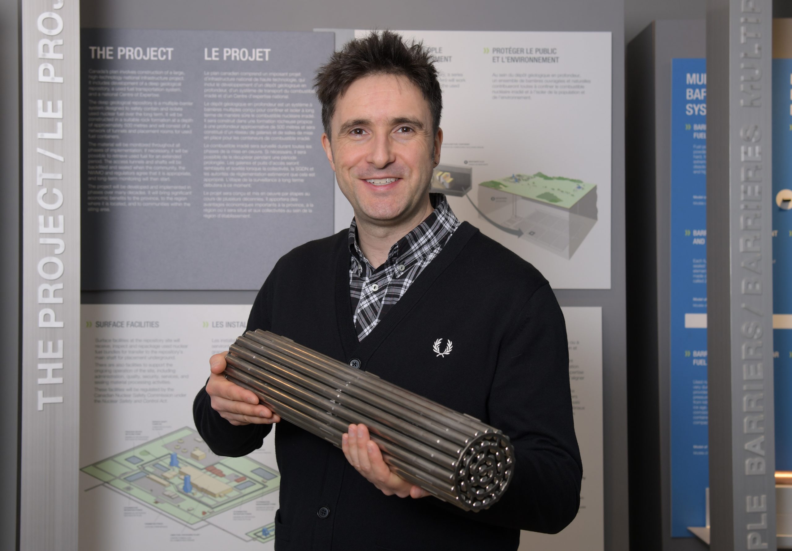 A man stands in front of information boards and holds a cylindrical model