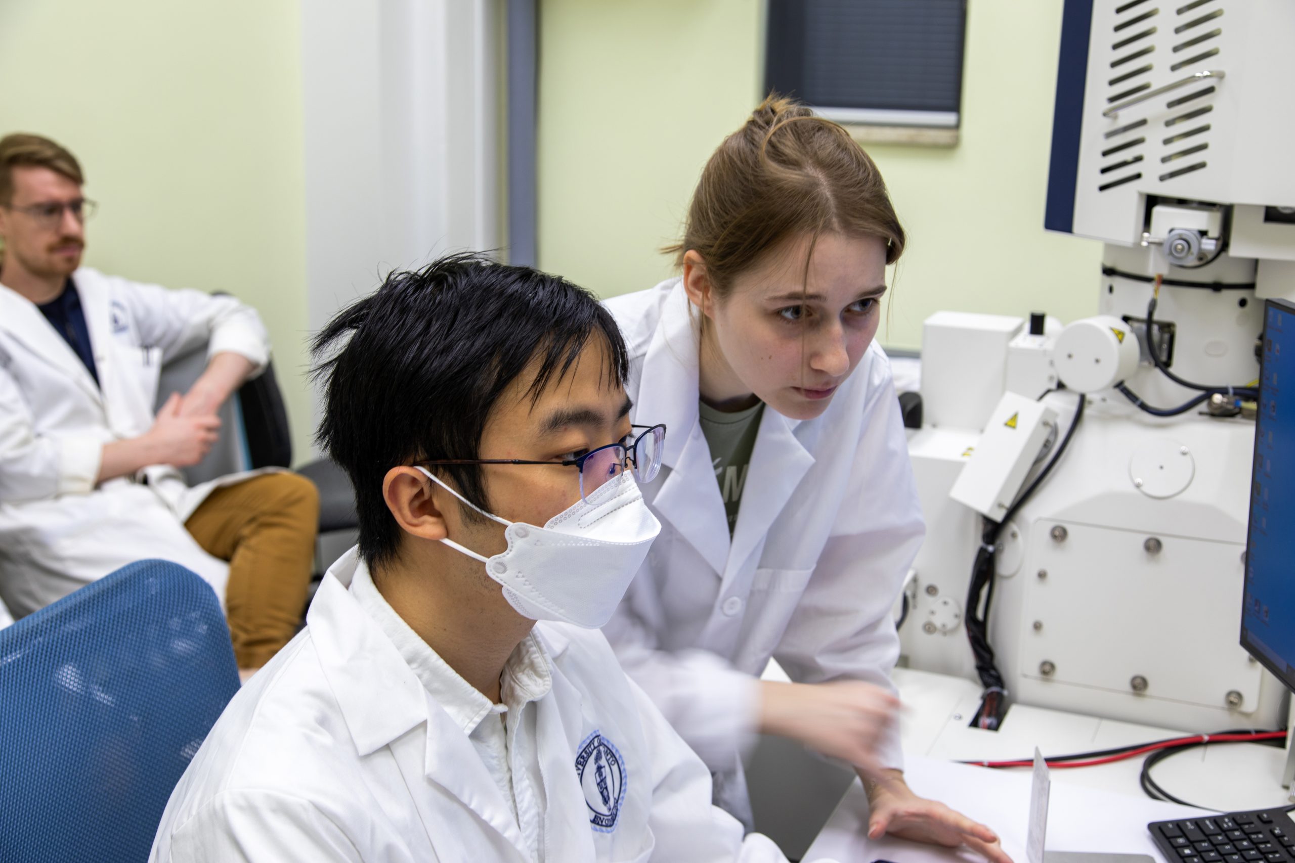Two researchers appear focused on a computer monitor connected to the scanning electron microscope.