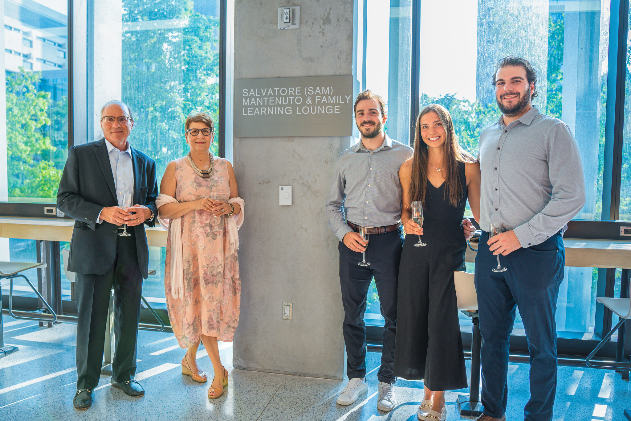 five individuals stand around a pillar with a sign that reads "Salvatore (Sam) Mantenuto & Family Learning Lounge." They are facing forward with windows behind them. From left to right: Sam Mantenuto (ECE 8T0, MBA 1990), Zaira Mantenuto, Daniel Mantenuto, Thalia Zolis, Michael Mantenuto.
