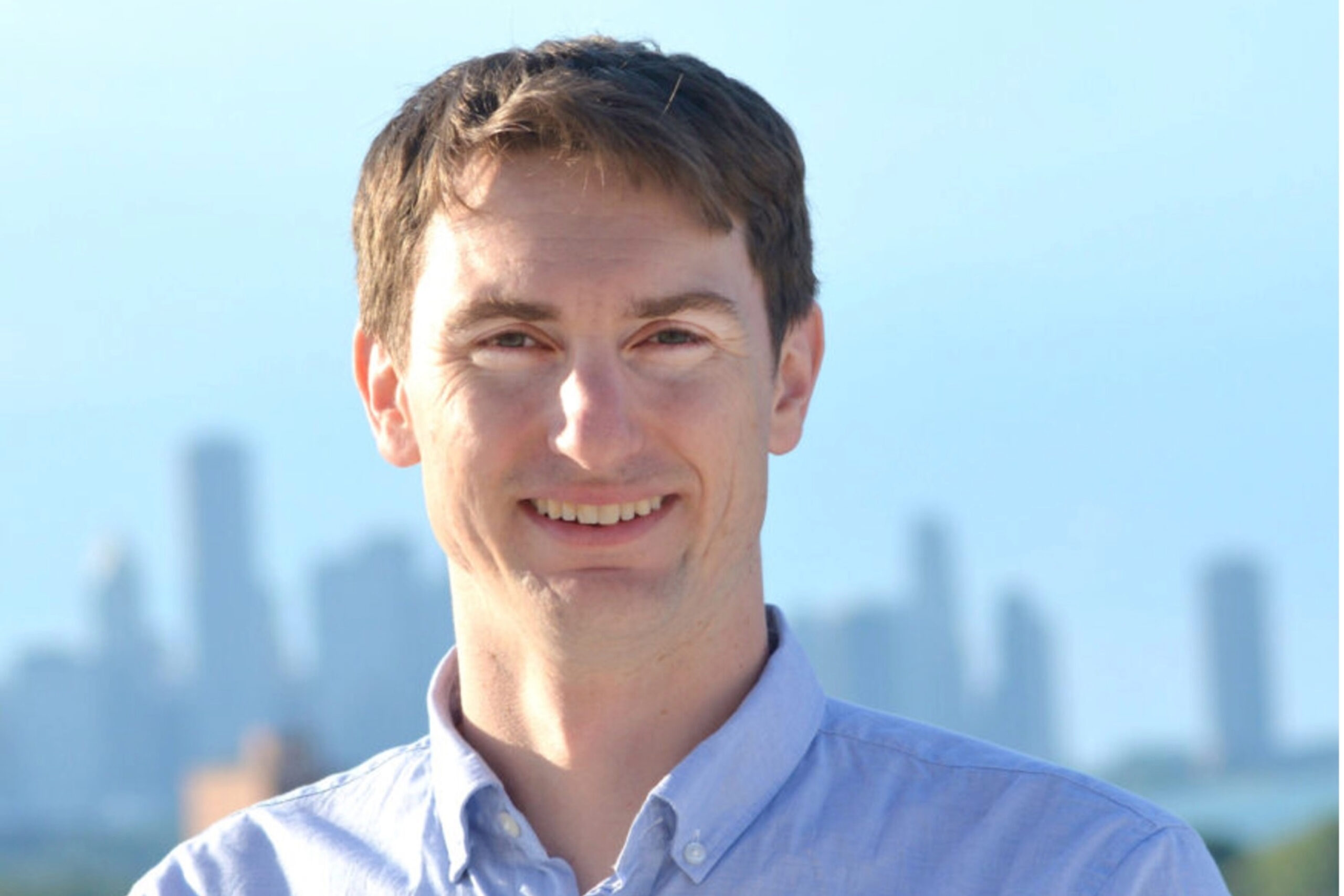 Trevor Carey is photographed from the shoulders up. A city scape is seen in the background.