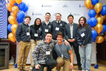 A group photos of 7 students with Dean Chris Yip in front of a banner flanked by balloons.