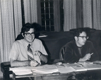 black and white photos of two students at a table with papers across it