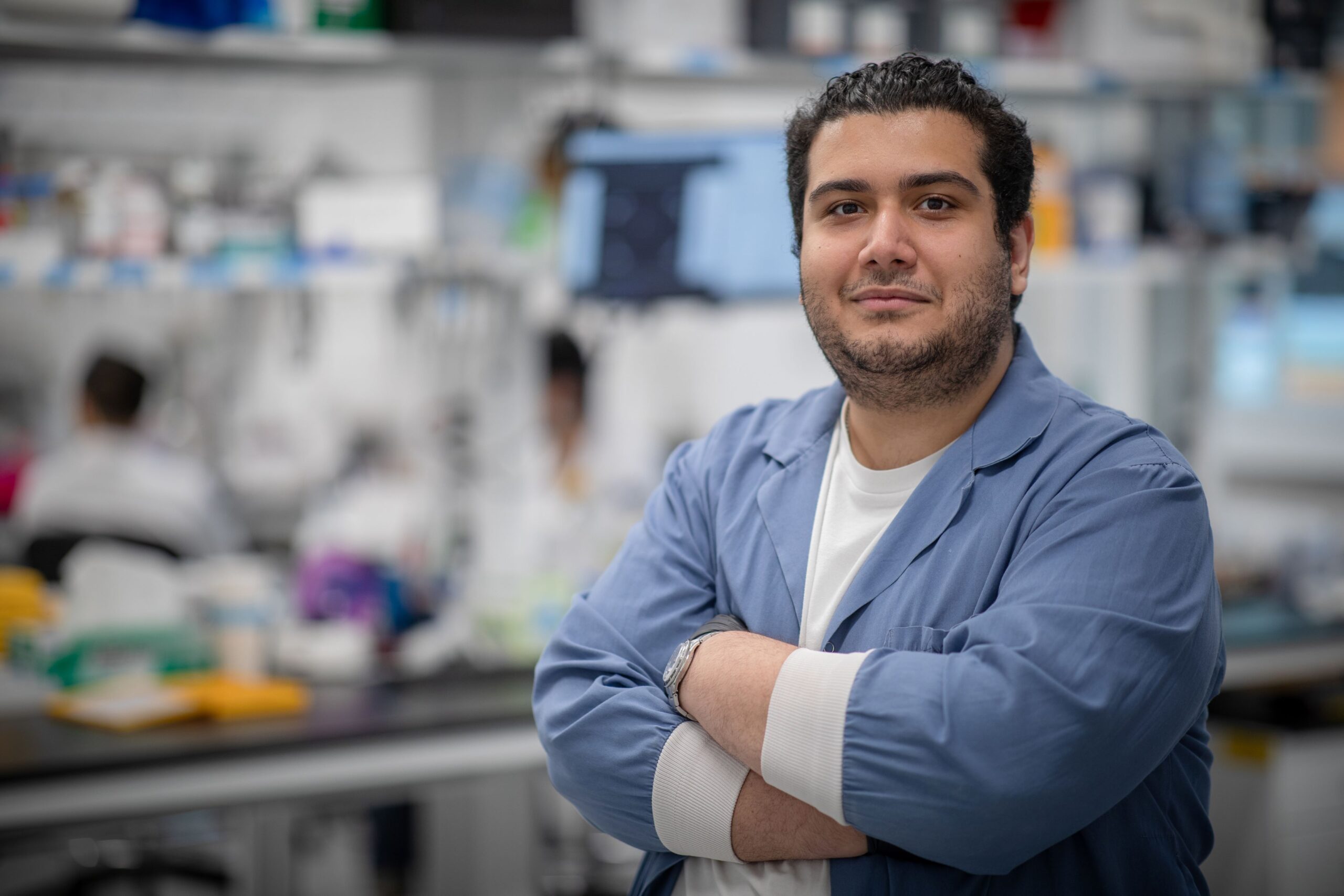 Moghaddam stands with his arms crossed, smiling at the camera, with lab equipment behind him