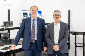 Doug and Afshin face the camera in front of an equipment work station