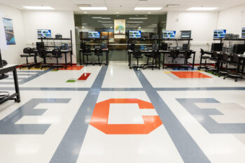A photo of the lab, with ECE print on the floor and equipment stations around the periphery of the room.