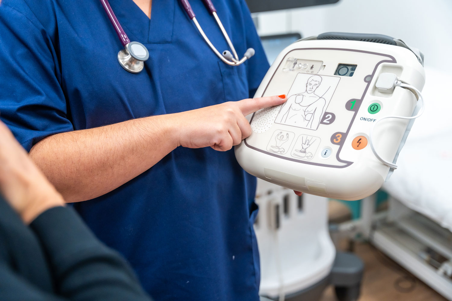 a medical practitioner wearing a stethoscope points at an AED