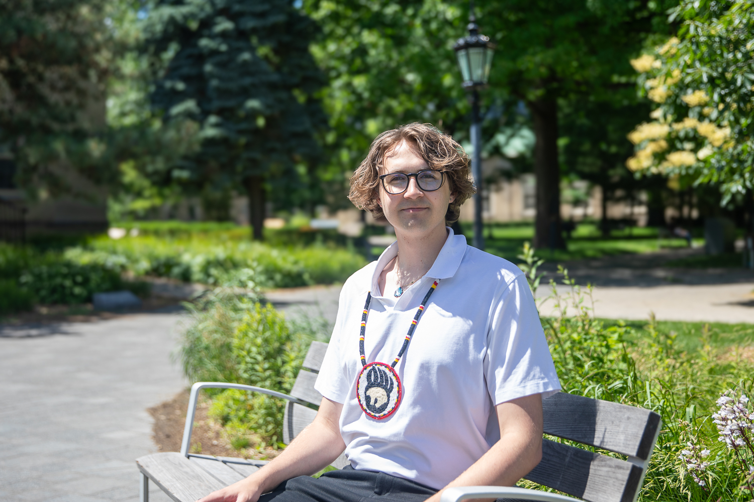 A person sits on a bench with greenery behind them.