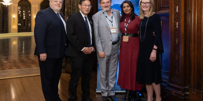 5 individuals stand in front of a banner for a photo together