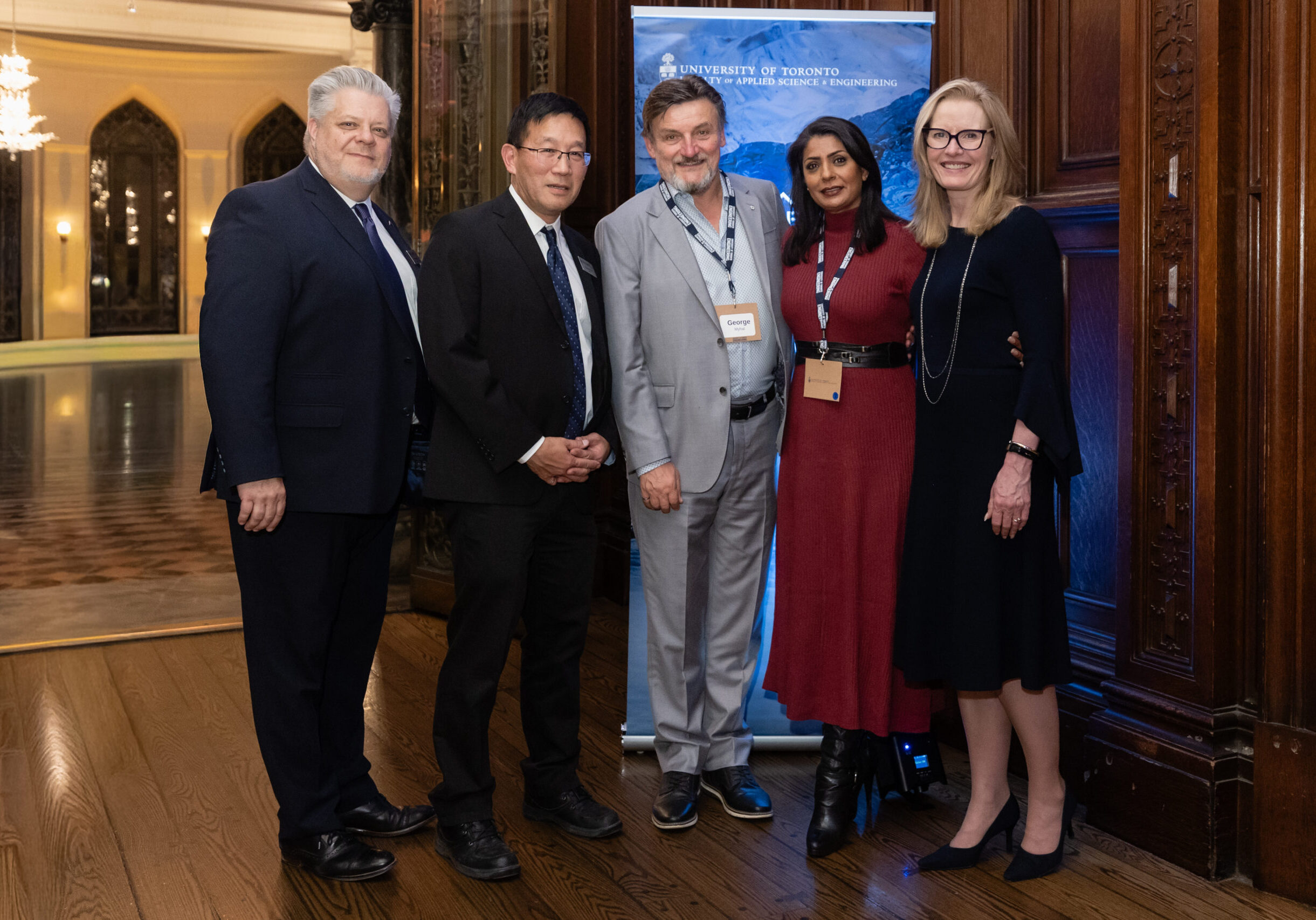 5 individuals stand in front of a banner for a photo together