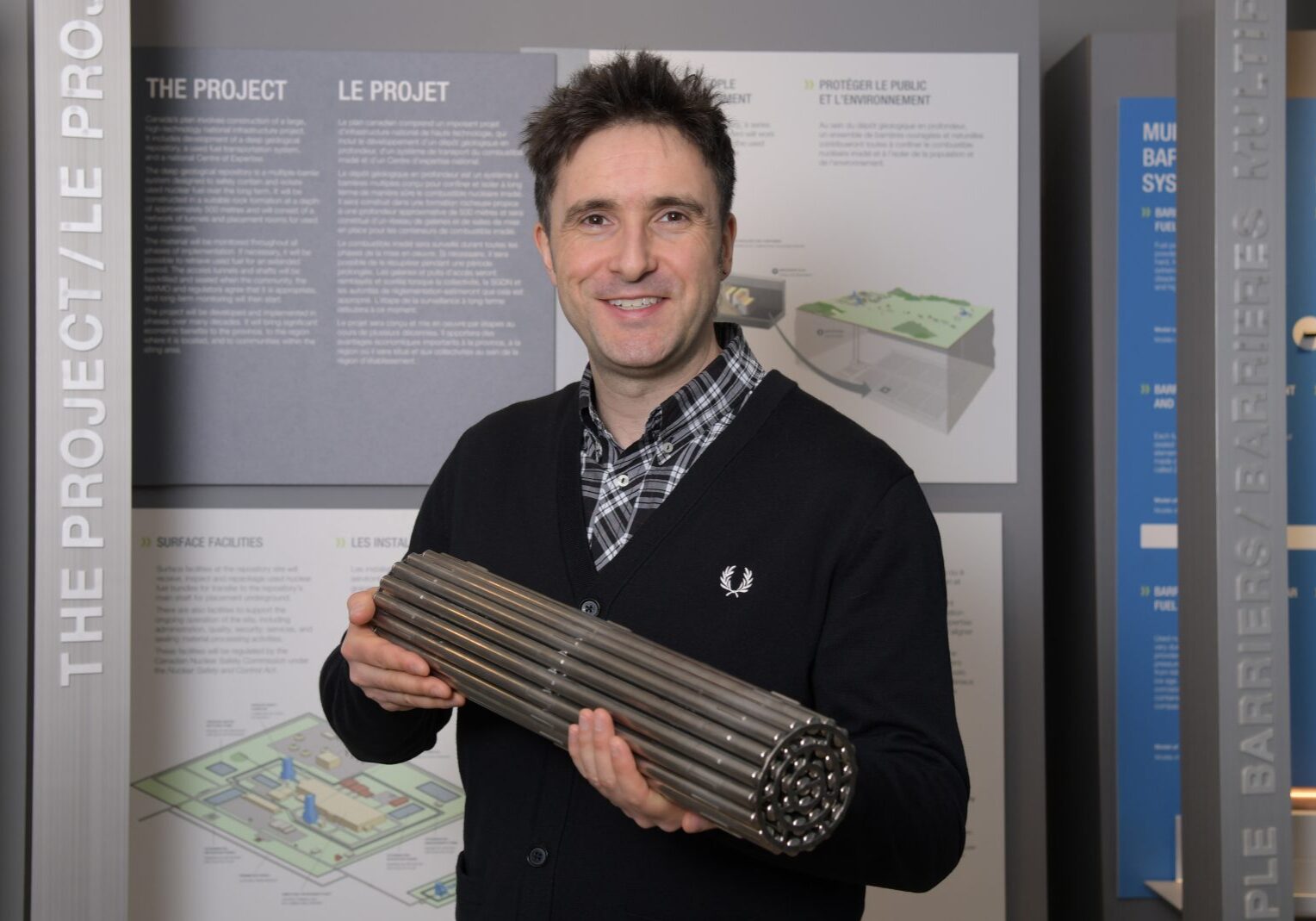 A man stands in front of information boards and holds a cylindrical model