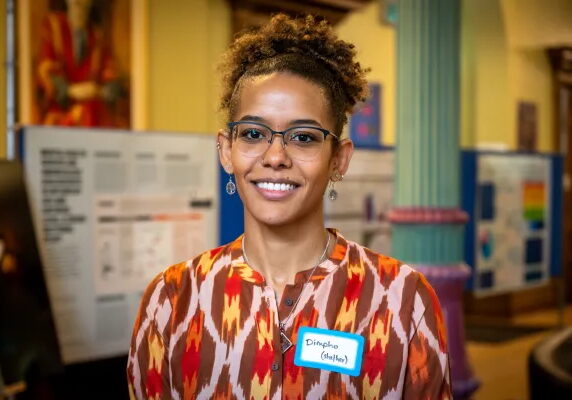 Dimple stands in front of poster presentation displays, smiling at the camera