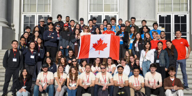 A large group of students pose on steps with a Canadian flag held in the middle of the group