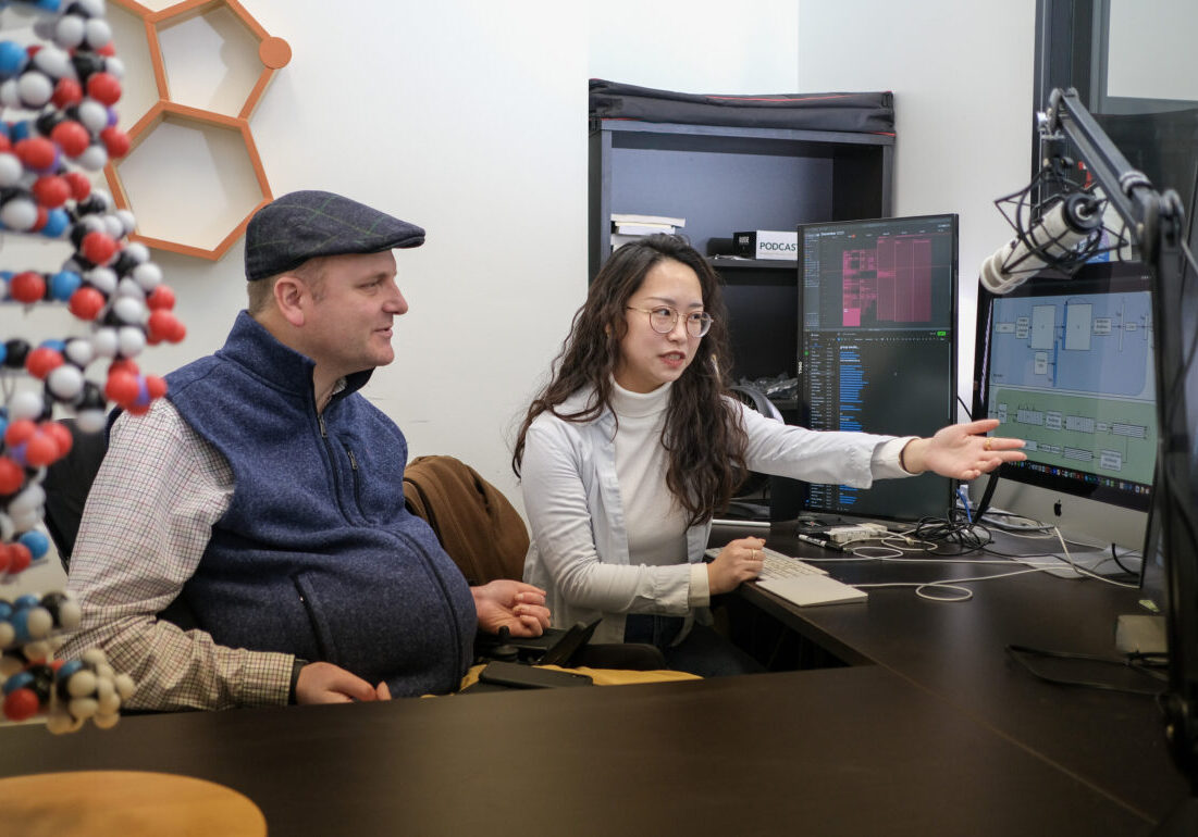 Two researchers seated before a computer station. The two appear to be focused on the data displayed on a monitor.