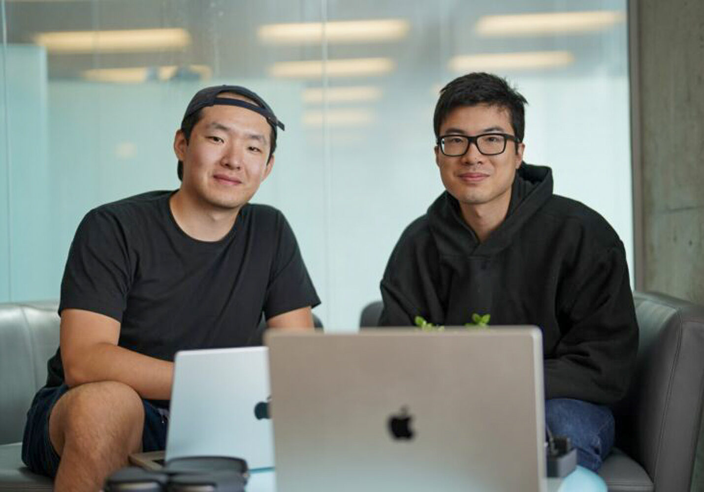 Left to right: Aaron Tan and Angus Fung sit behind their laptops in an office.