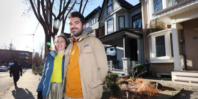 Saxe and Olson stand on the sidewalk of a street lined with houses