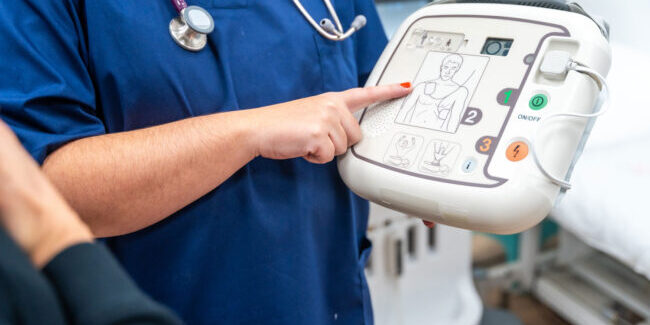 a medical practitioner wearing a stethoscope points at an AED