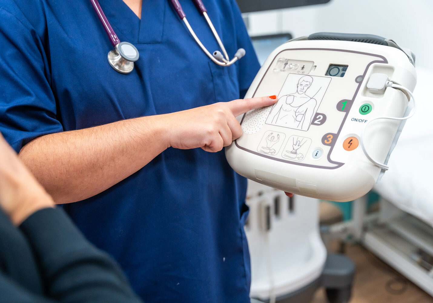 a medical practitioner wearing a stethoscope points at an AED